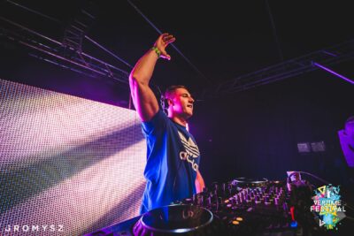 DJ z uniesioną ręką za konsolą podczas festiwalu przy ekranie LED