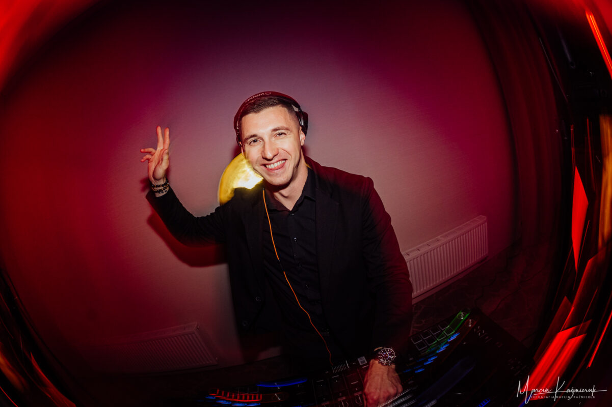 DJ Piotr Wiater miksujący za konsolą podczas imprezy – klubowe oświetlenie