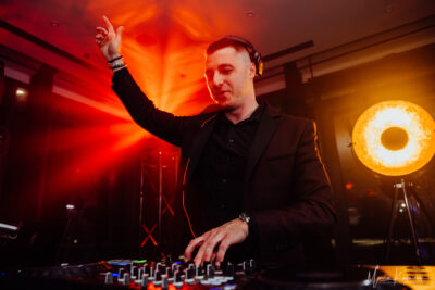 DJ Piotr Wiater za konsolą podczas wesela – elegancki garnitur, ciepłe światła parkietu