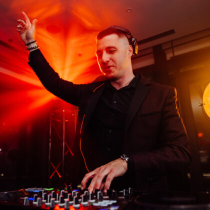 DJ Piotr Wiater za konsolą podczas wesela – elegancki garnitur, ciepłe światła parkietu